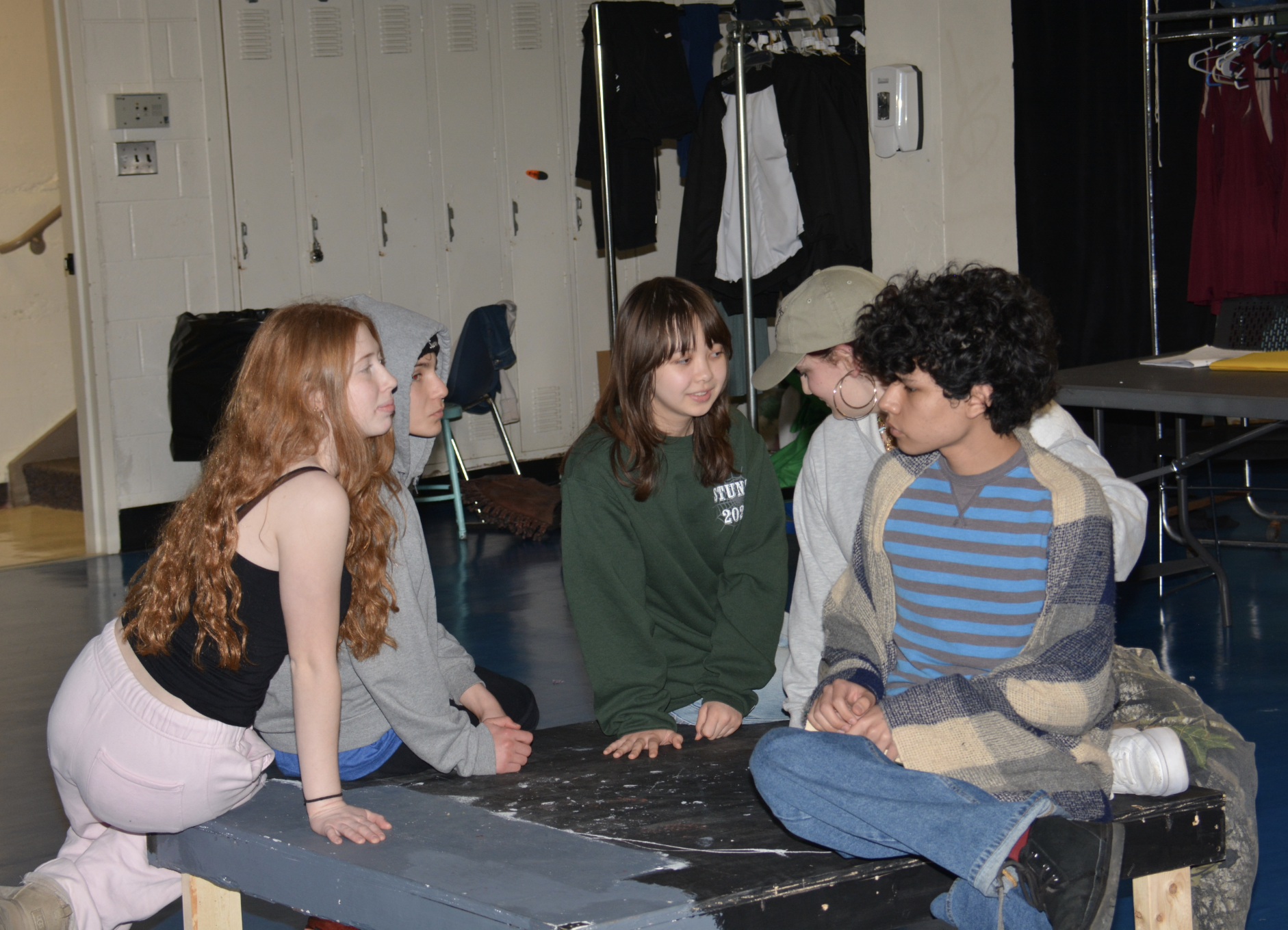 2026 - Actors sit on low leveled table on stage. Pictured left to right: Mazzy Egenthal (Tom Snout the Tinker), Dylan Poll (Francis Flute the Bellows-mender), Olivia Rejano (Snug the Joiner), Josie Wolfe (Peter Quince the Carpenter), & Javier Pulido (Robin Starveling the Tailor).
